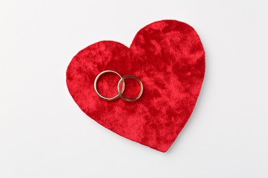 Photo of Honeymoon concept. Red velvet heart and two golden rings on white background, top view