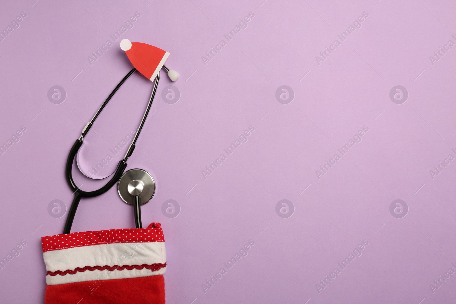 Photo of Greeting card for doctor with stethoscope and Christmas decor on purple background, flat lay. Space for text