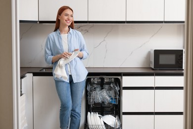 Photo of Smiling woman wiping plate near open dishwasher in kitchen