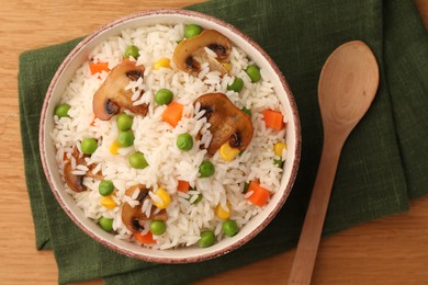 Bowl of delicious rice with vegetables on wooden table, top view