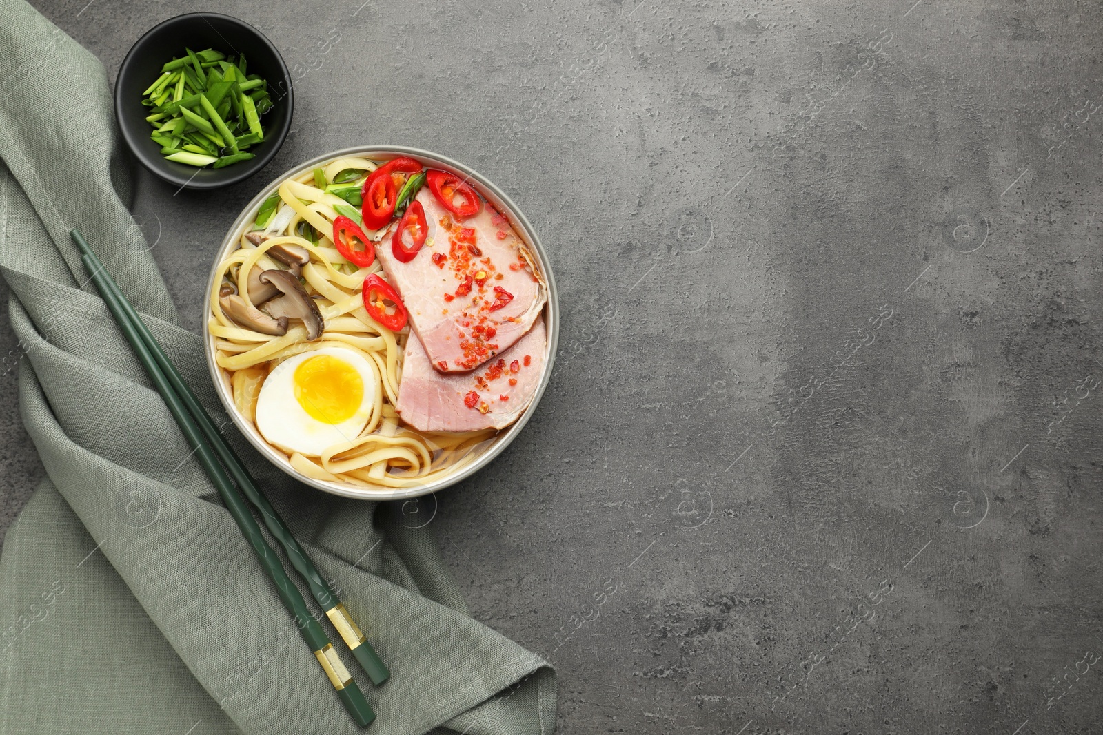 Photo of Delicious ramen in bowl served on grey textured table, flat lay and space for text. Noodle soup