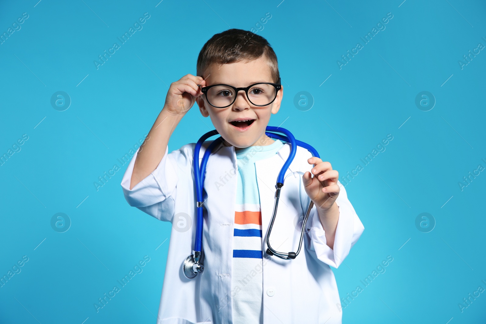 Photo of Cute child in doctor coat with stethoscope on color background