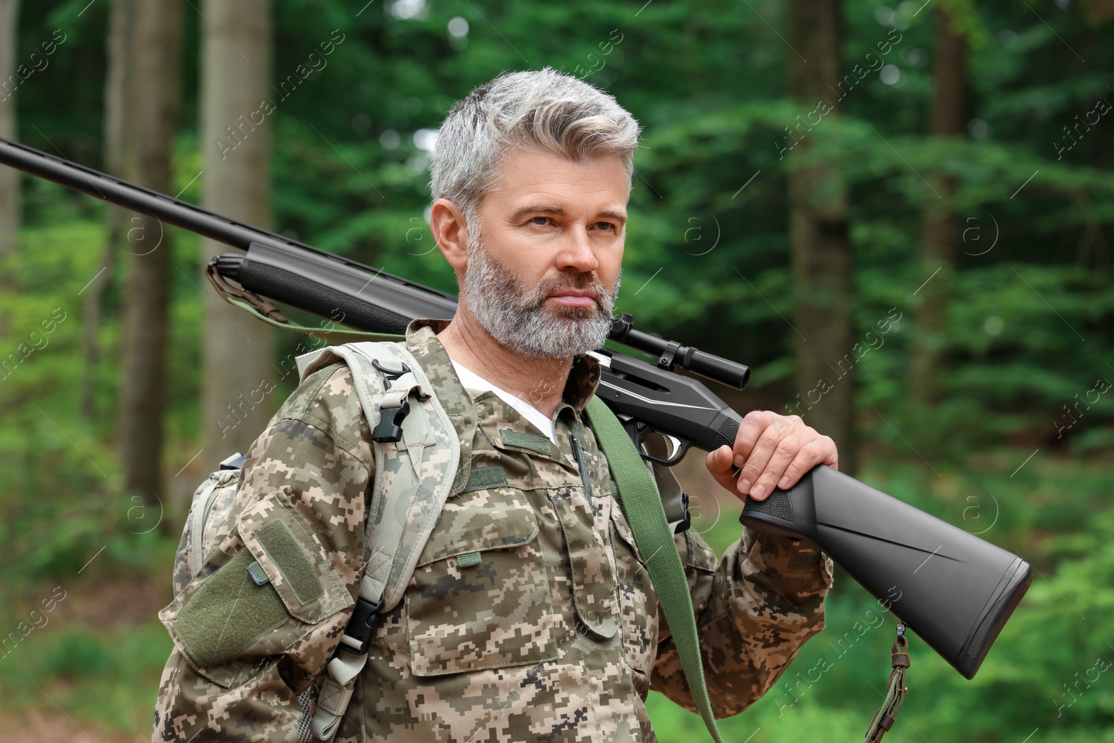 Photo of Man with hunting rifle and backpack wearing camouflage in forest