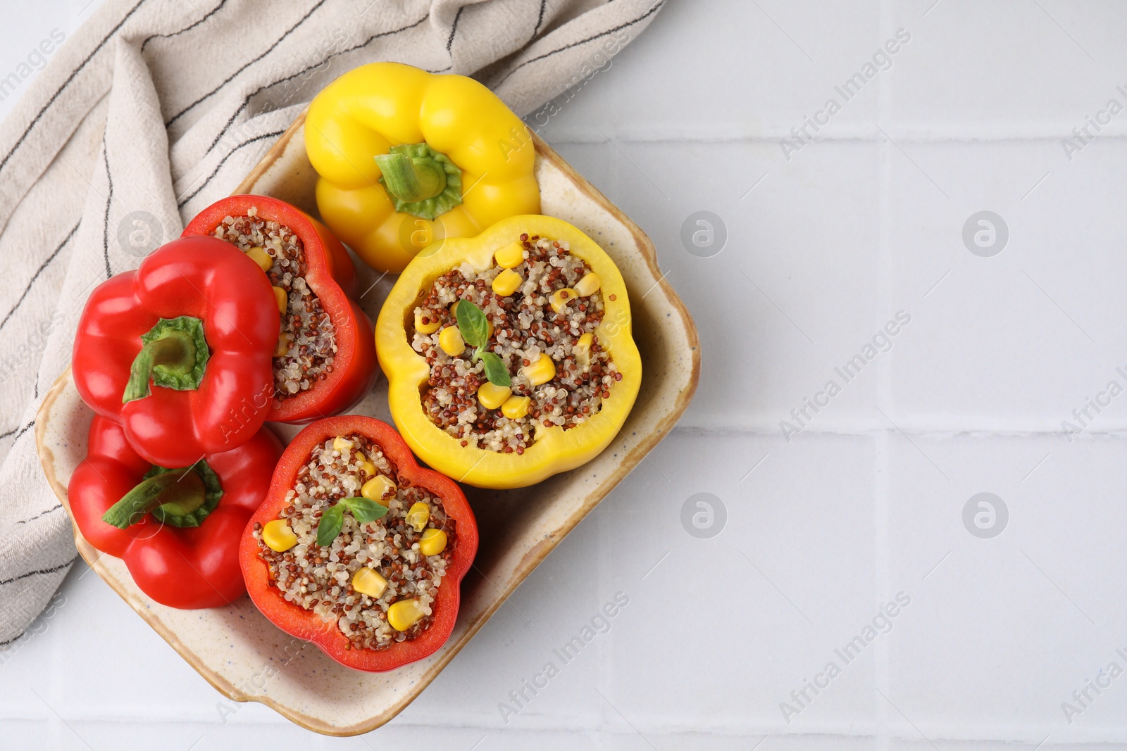 Photo of Quinoa stuffed bell peppers and basil in baking dish on white tiled table, top view. Space for text