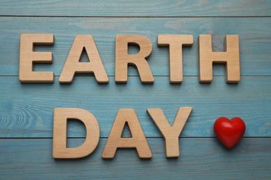 Photo of Words Earth Day made of wooden letters and decorative heart on turquoise table, flat lay