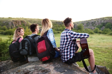 Group of young people with backpacks and guitar in wilderness. Camping season