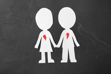 Photo of Human paper figures with parted heart on black stone background, flat lay. Composition symbolizing problems in relationship