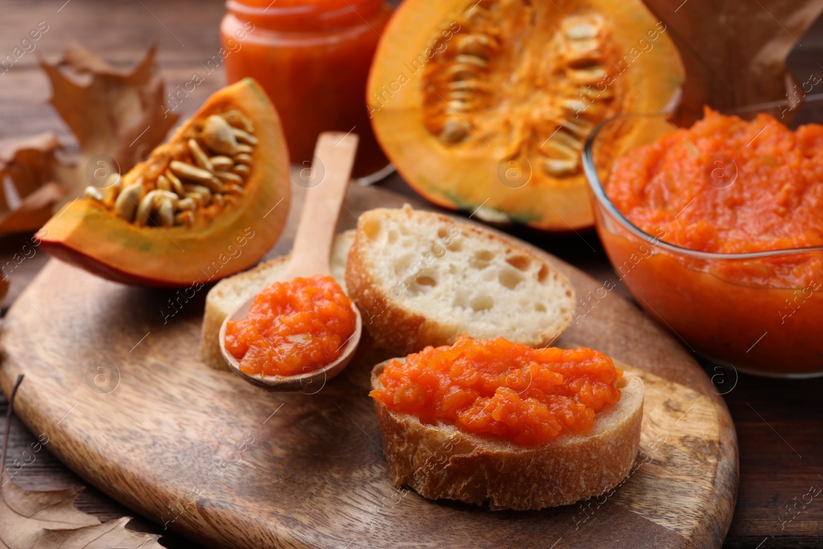 Photo of Slices of bread with delicious pumpkin jam and fresh pumpkin on wooden table, closeup