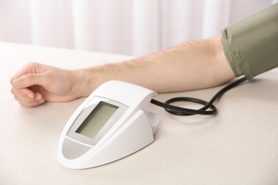 Photo of Man checking pulse and blood pressure with sphygmomanometer on table, closeup