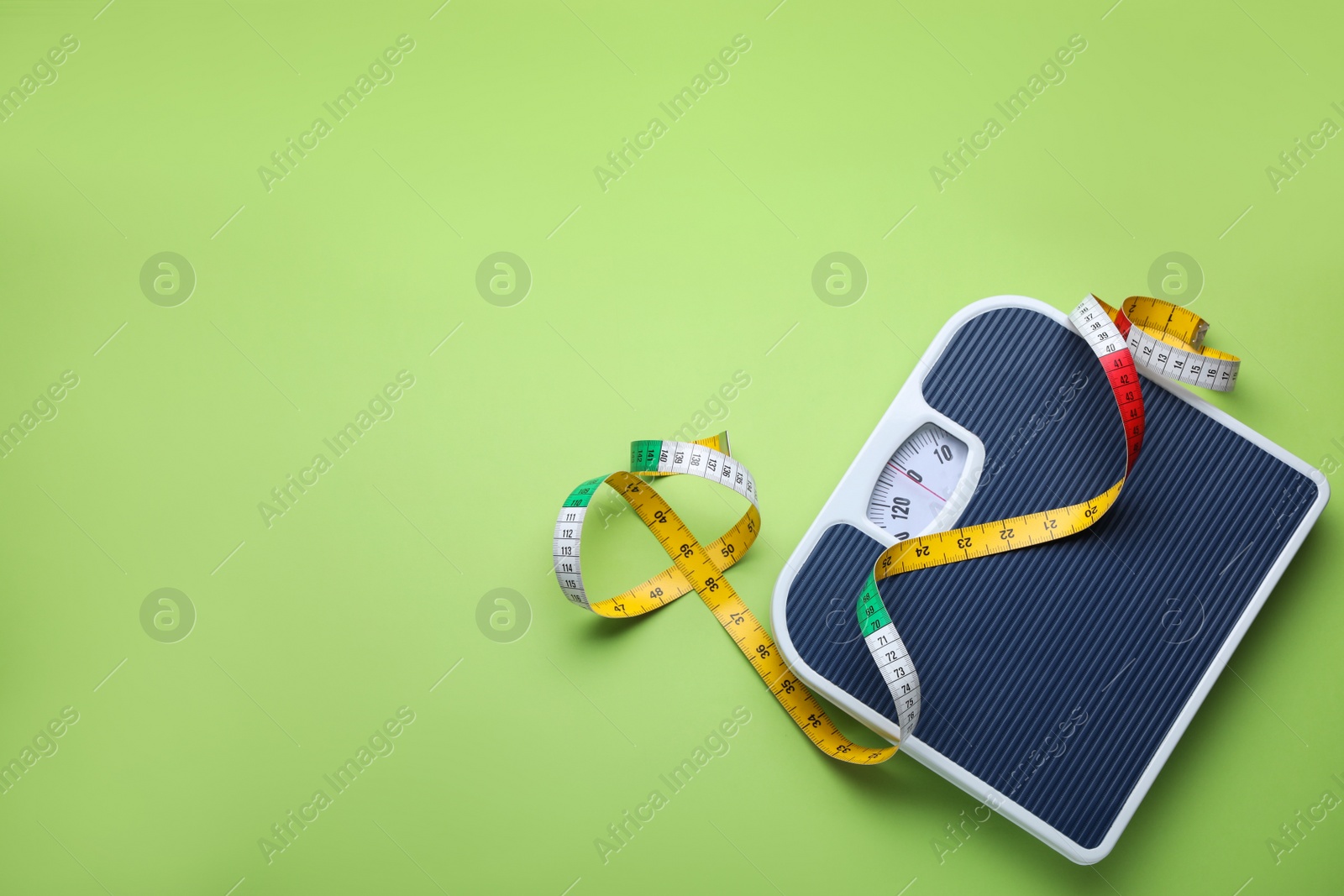 Photo of Scales and measuring tape on green background, flat lay. Space for text