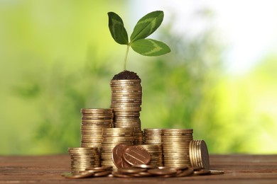 Stacked coins and green sprout on wooden table against blurred background. Investment concept