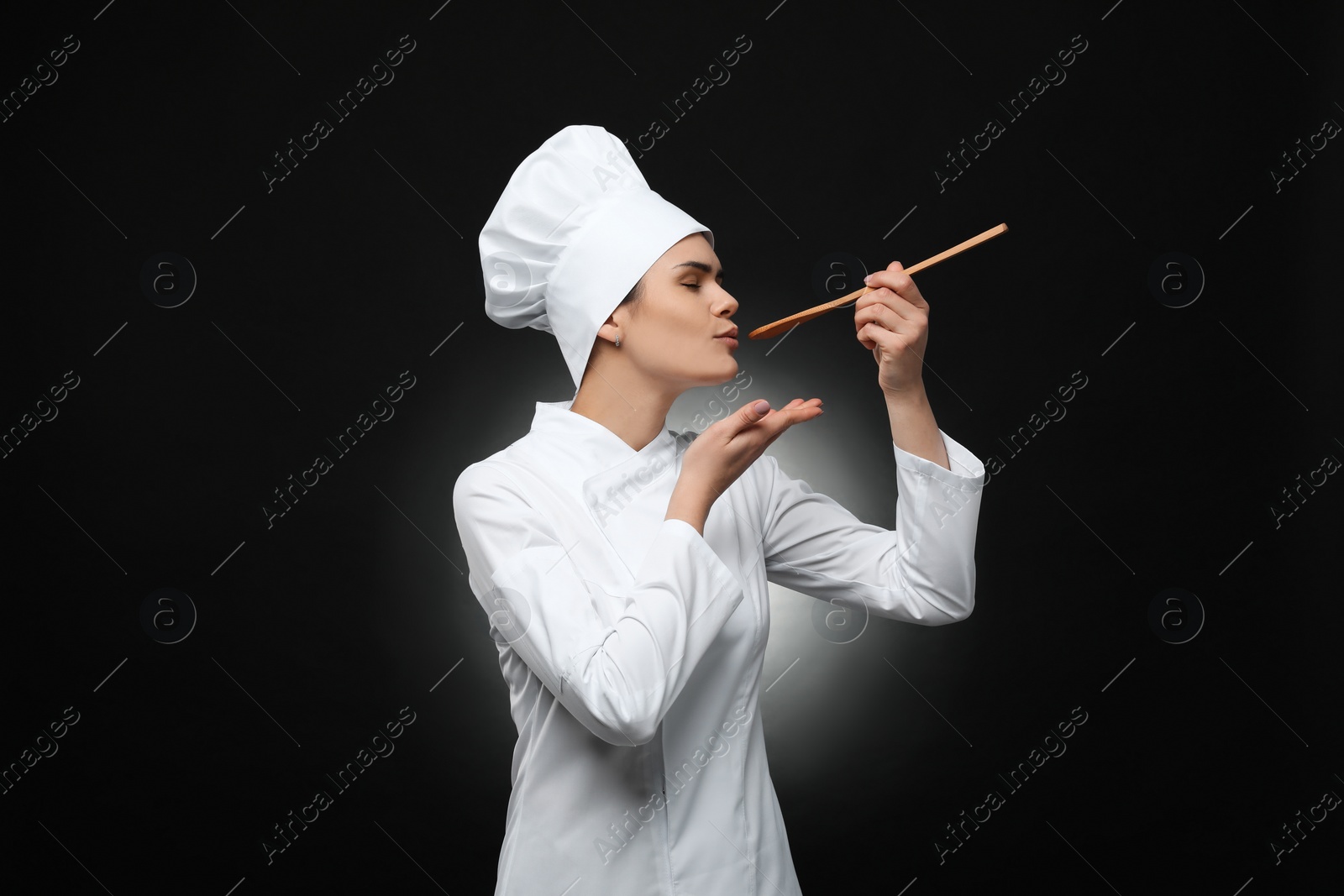 Photo of Happy female chef tasting something on black background