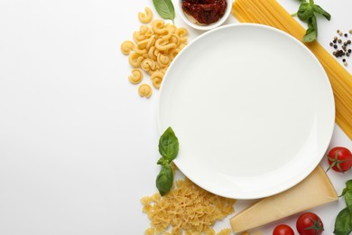 Photo of Plate surrounded by different types of pasta, products and peppercorns on white background, flat lay. Space for text