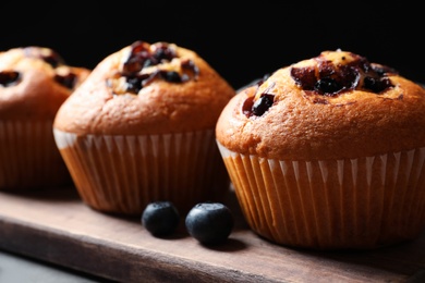 Photo of Tasty blueberry muffins on wooden board against black background, closeup view