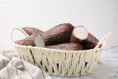 Whole and cut cassava roots in wicker basket on white marble table