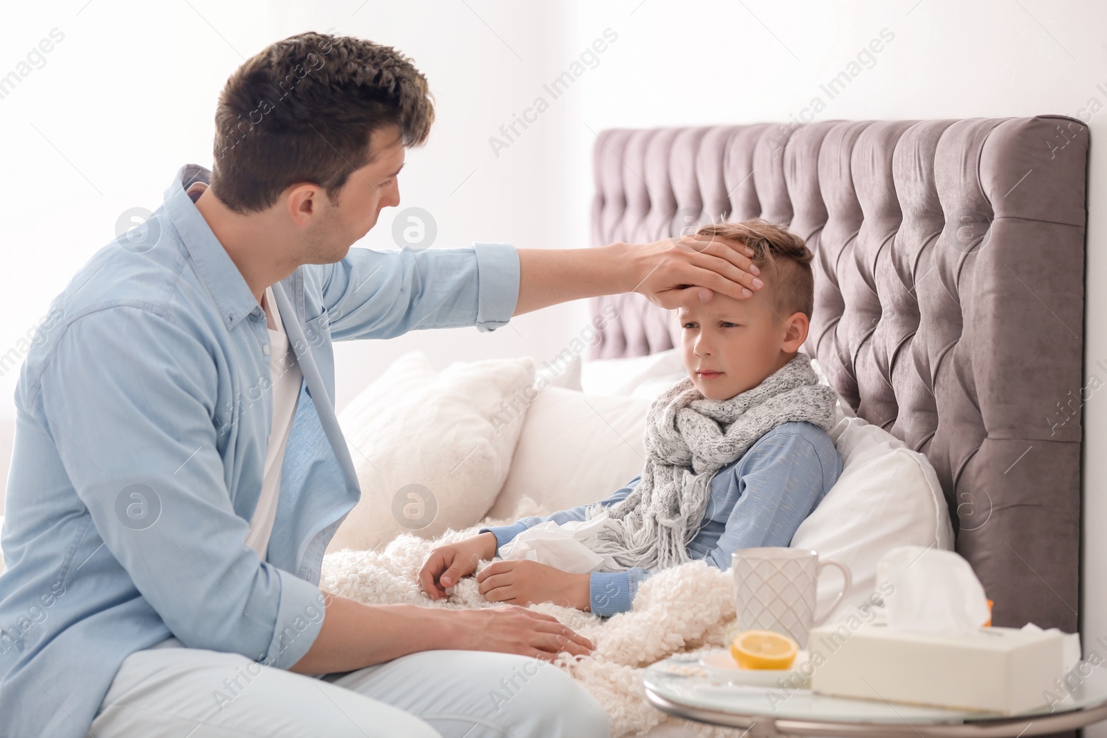 Photo of Father taking care of little son suffering from cold in bed