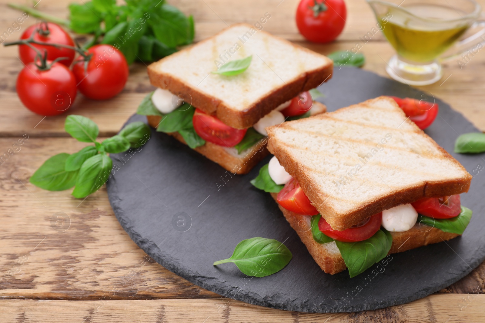 Photo of Delicious Caprese sandwiches with mozzarella, tomatoes, basil and pesto sauce on wooden table