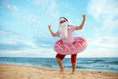 Santa Claus with inflatable ring having fun on beach, space for text. Christmas vacation