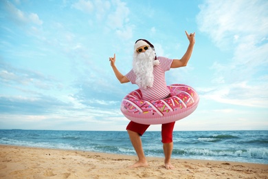 Photo of Santa Claus with inflatable ring having fun on beach, space for text. Christmas vacation