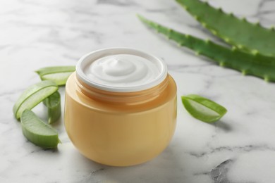 Jar with cream and cut aloe leaves on white marble table, closeup