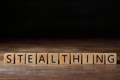 Image of Word Stealthing of cubes on wooden table against black background. Space for text