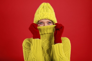 Funny young woman in warm sweater, gloves and hat on red background. Winter season