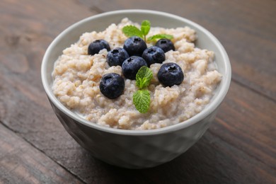 Delicious barley porridge with blueberries and mint in bowl on wooden table, closeup