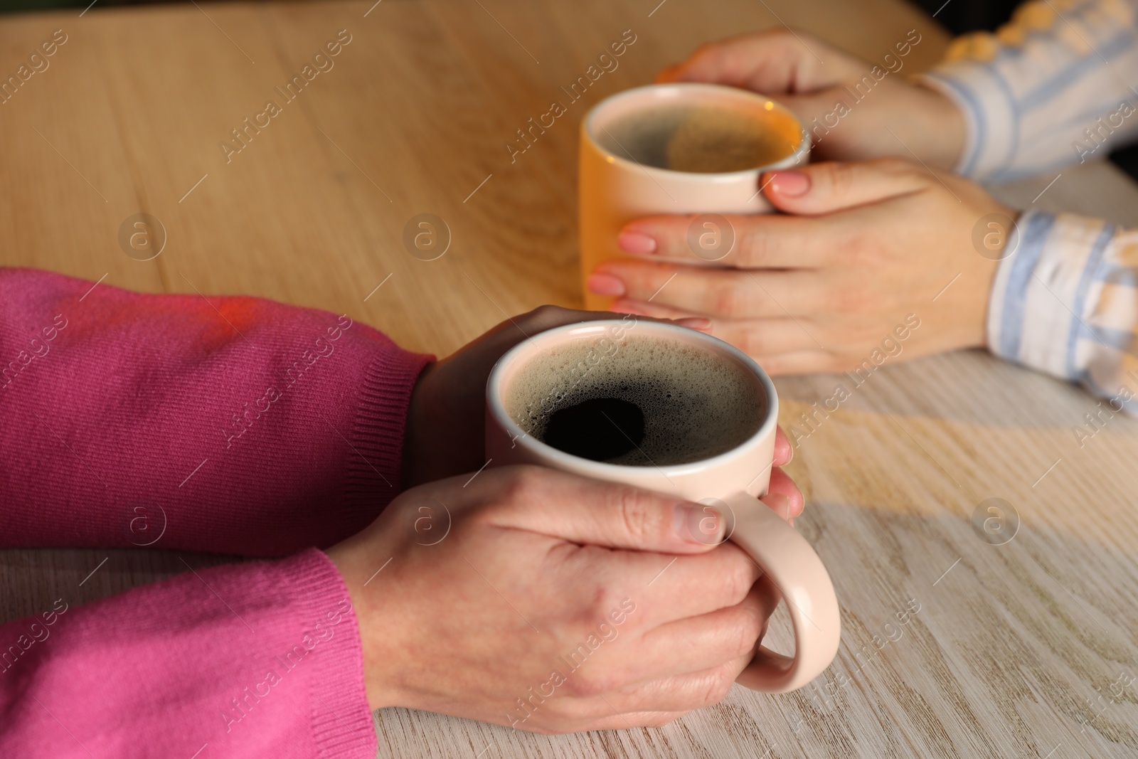 Photo of Women with cups of hot coffee at light wooden table, closeup