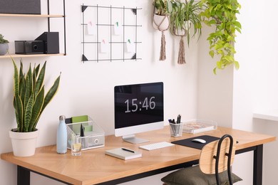 Photo of Cozy workplace with computer, modern furniture and houseplants at home