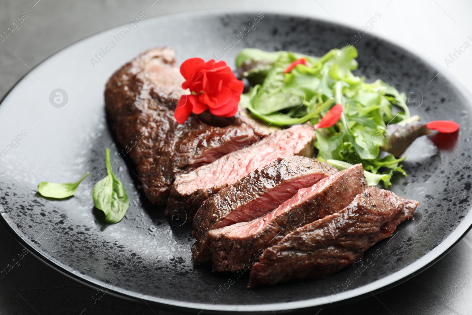 Photo of Pieces of delicious grilled beef meat and greens on table, closeup