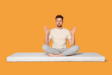 Photo of Man sitting on soft mattress and meditating against orange background