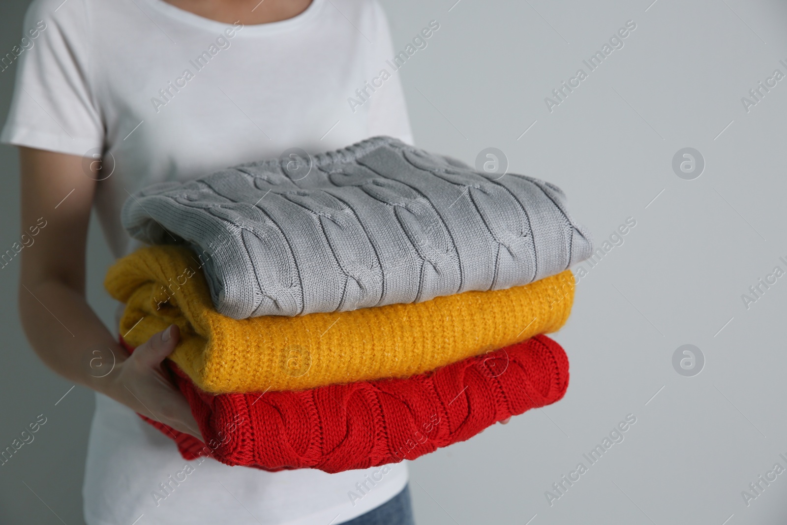 Photo of Woman with stack of knitted sweaters on grey background, closeup