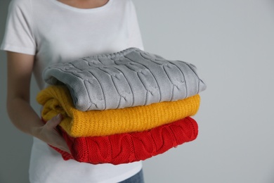 Photo of Woman with stack of knitted sweaters on grey background, closeup