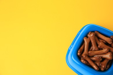 Blue bowl with bone shaped dog cookies on yellow background, above view. Space for text