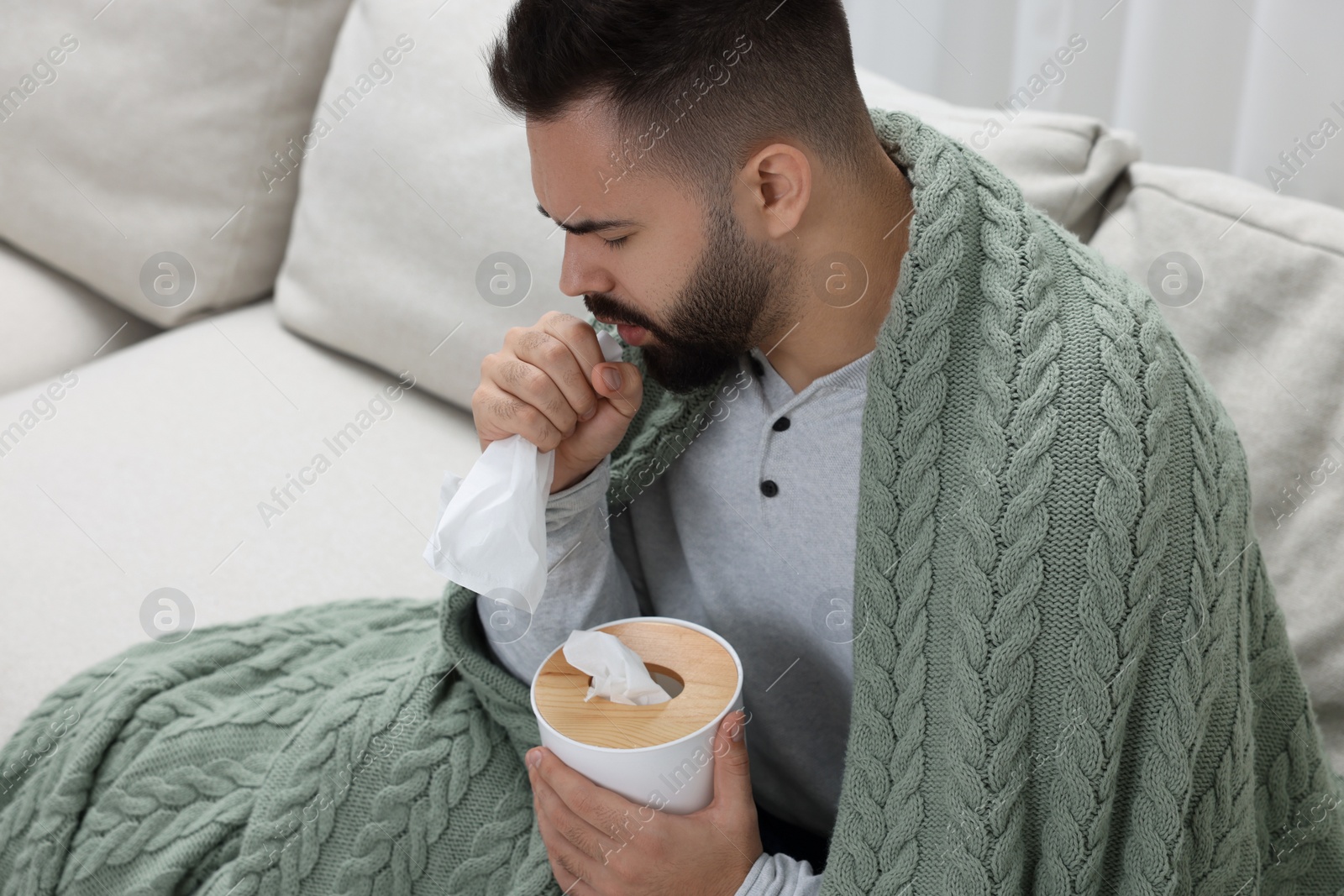 Photo of Sick man with tissue coughing at home