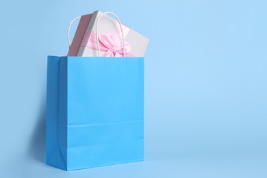Photo of Bright paper shopping bag with gift box on light blue background. Space for text