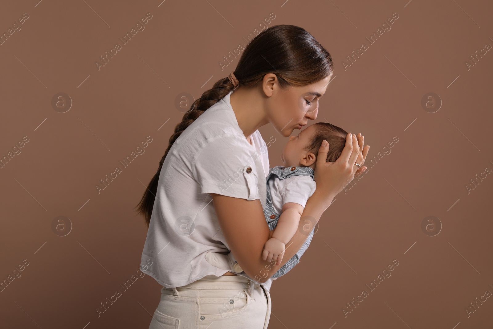 Photo of Mother kissing her cute newborn baby on brown background