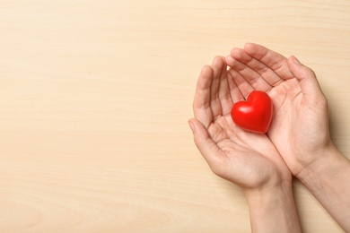 Woman holding heart on wooden background, top view with space for text. Donation concept