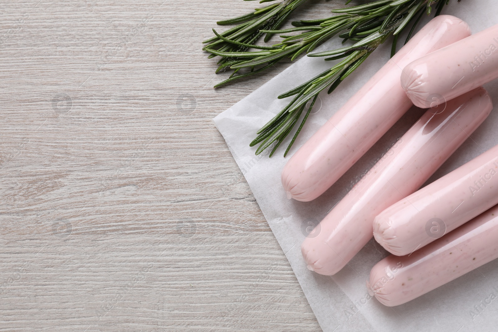 Photo of Vegan sausages and rosemary on white wooden table, flat lay. Space for text