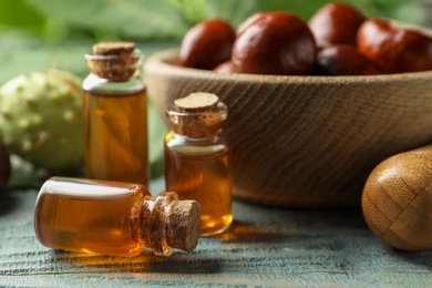 Photo of Mortar with pestle, chestnuts and bottles of essential oil on blue wooden table, closeup