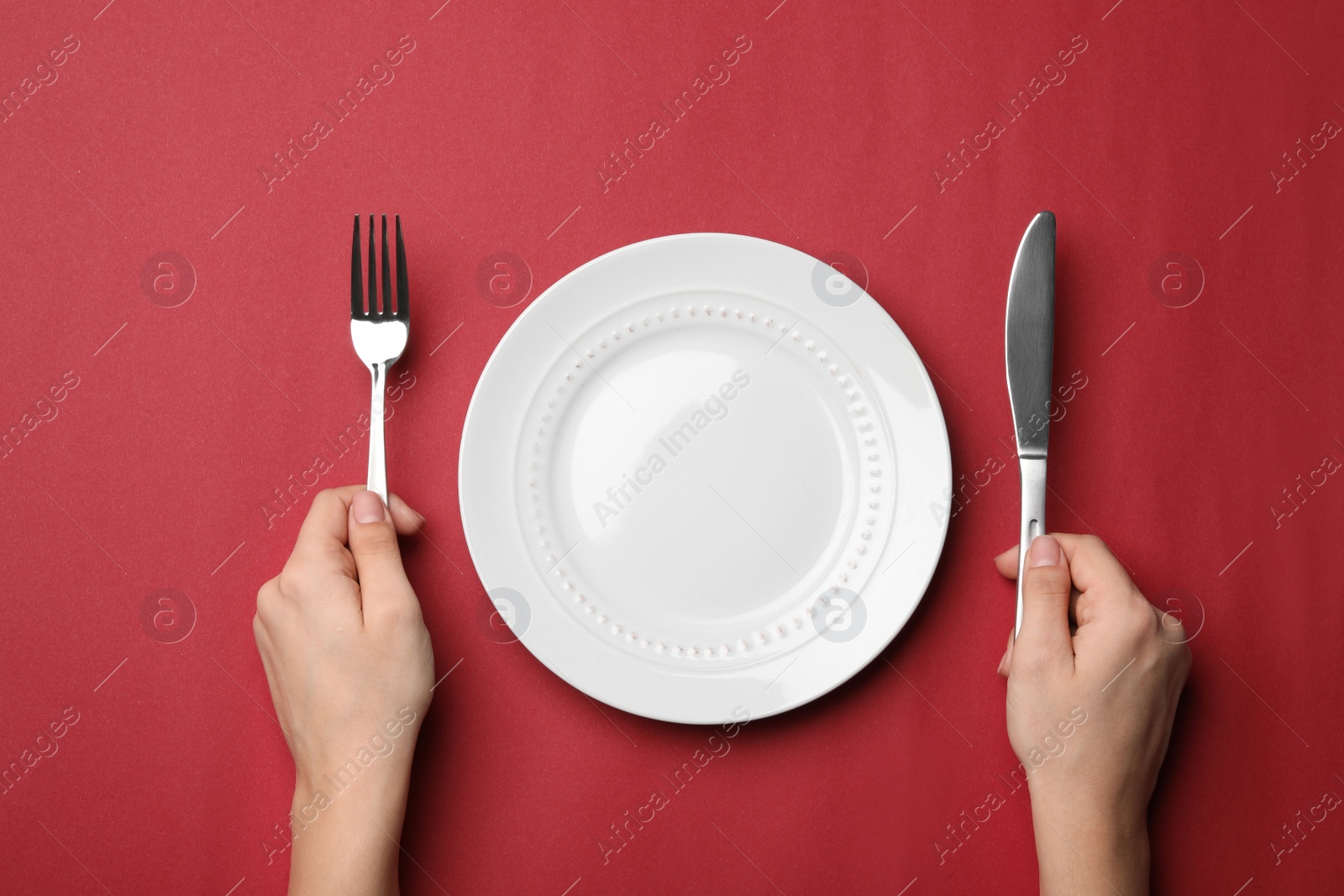 Photo of Woman with fork, knife and empty plate on color background, top view