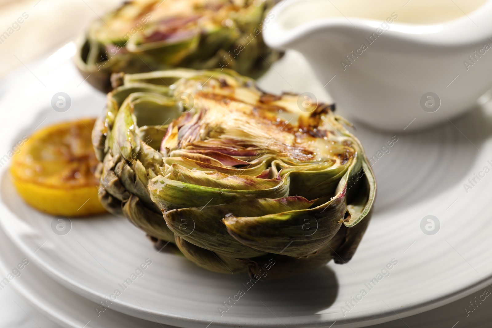 Photo of Tasty grilled artichokes on plate, closeup view