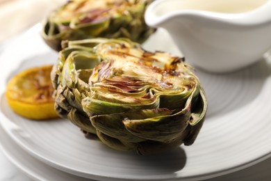 Photo of Tasty grilled artichokes on plate, closeup view