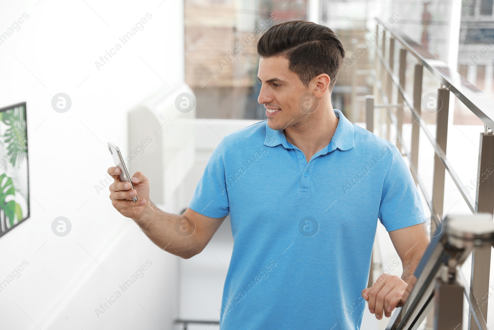 Photo of Portrait of handsome man with mobile phone on stairs in room
