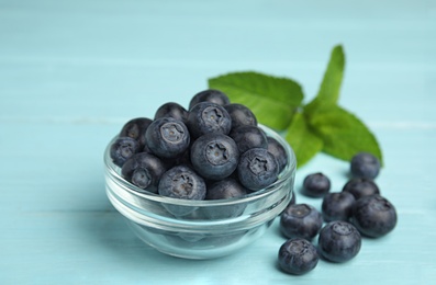 Photo of Glass bowl of tasty blueberries on color wooden table