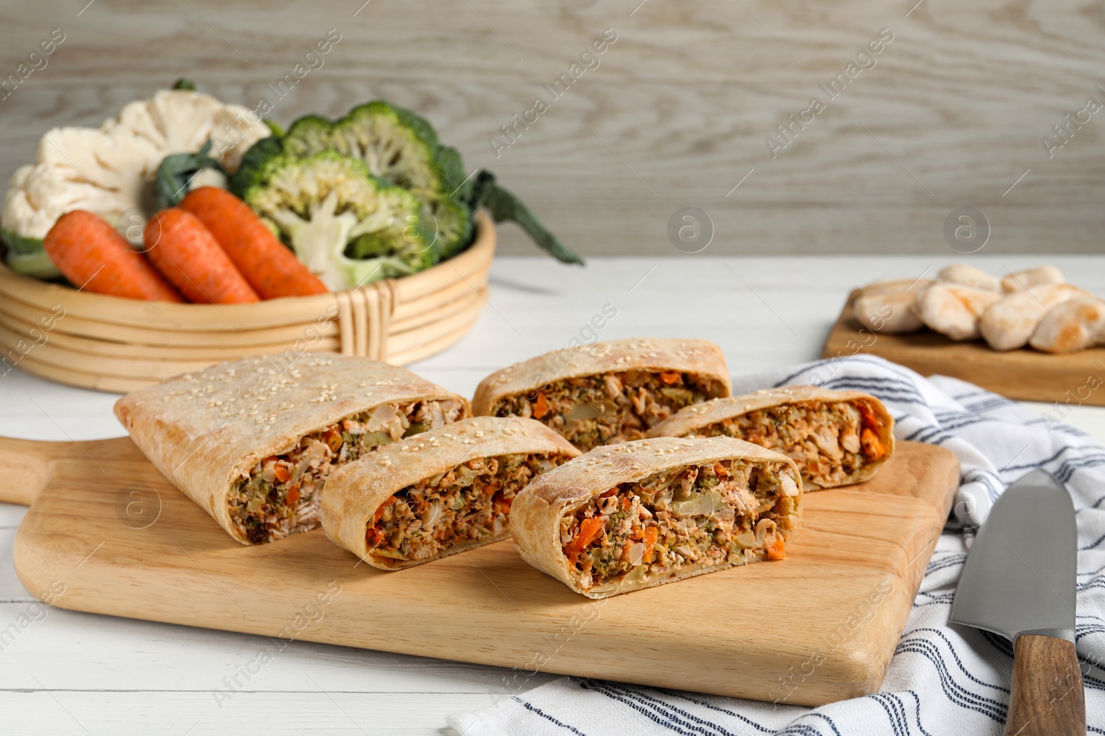 Photo of Cut tasty strudel with chicken, vegetables and knife on white wooden table