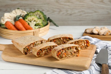 Cut tasty strudel with chicken, vegetables and knife on white wooden table