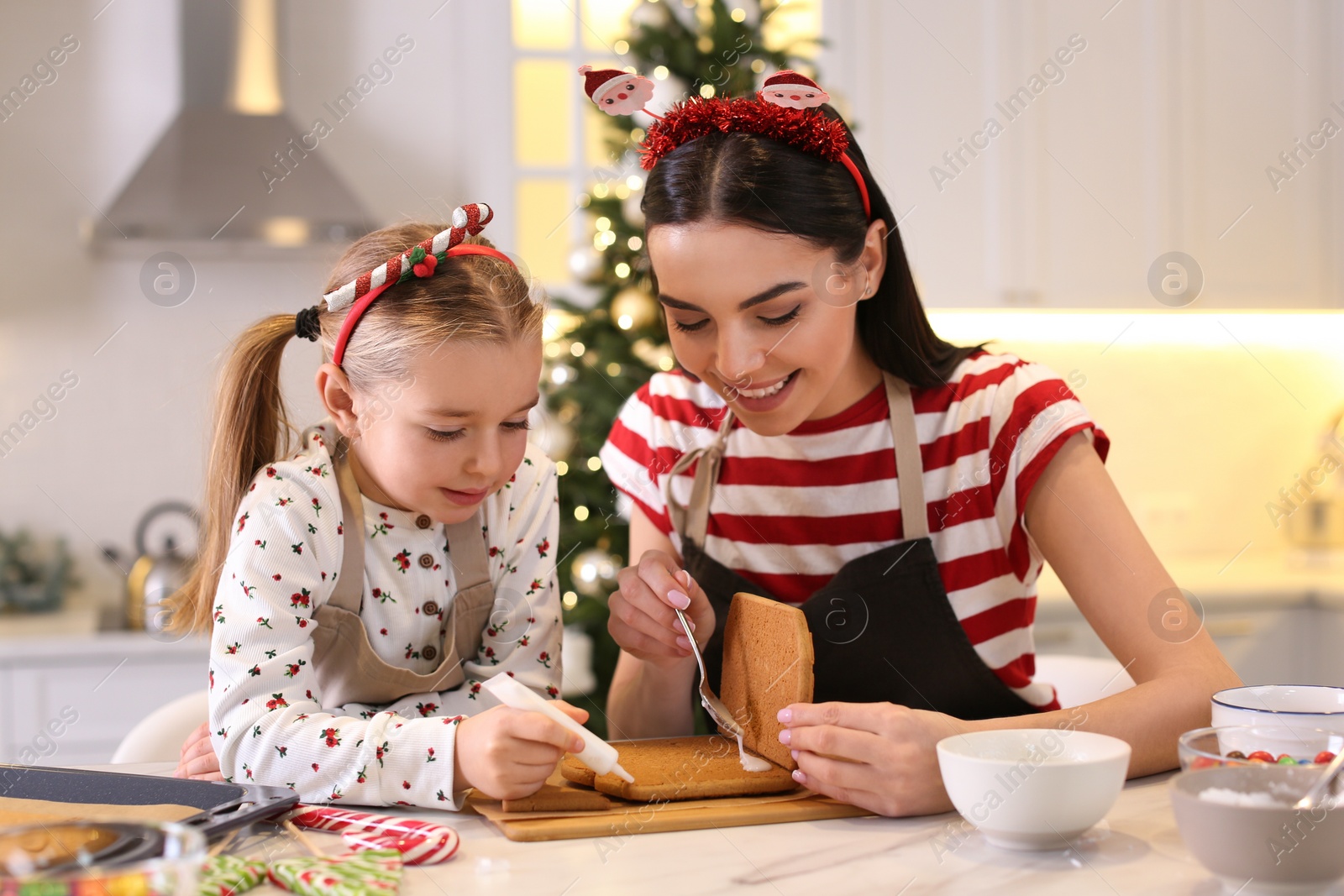 Photo of Mother and daughter making gingerbread house at table indoors