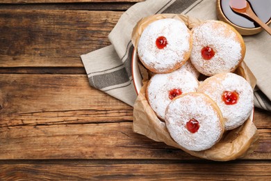 Photo of Delicious donuts with jelly and powdered sugar in baking dish on wooden table, flat lay. Space for text