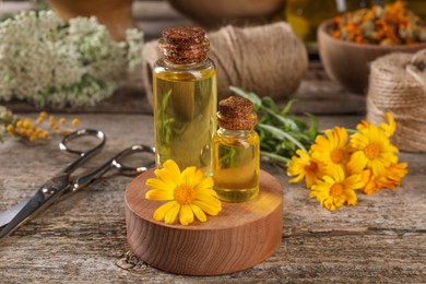 Photo of Bottles of essential oils, calendula flower and scissors on wooden table. Medicinal herbs